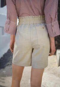 Shorts en lin beige avec une large ceinture élastique, dotés d'une poche arrière et d'une texture subtile. Associés à un blouse rayée rouge et blanche.
