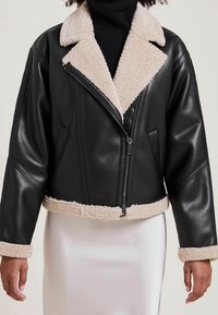 Czarna skórzana kurtka cropped z beżowym kołnierzem i dołem z owczej wełny. Posiada zamek błyskawiczny z przodu i kieszenie po bokach. Dopasowana w luźnym kroju.