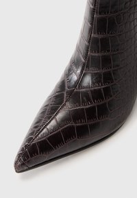 Bottine à bout pointu en cuir brun foncé à effet crocodile brillant ; elle présente une silhouette épurée et une texture lisse.
