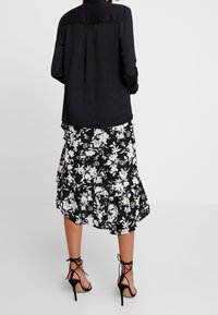 Musta pitkähihaine paita, jossa on nyörityksellä koristeltu yoke-osa, yhdistettynä musta-valkoiseen kukkakuosisia kietaisuhameeseen, jonka helmassa on röyhelöitä. Mustat korkokengät.