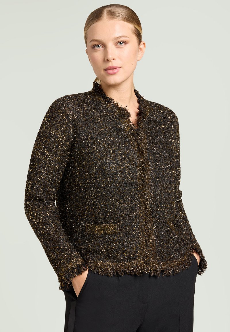 Black and gold textured jacket with a fringed collar and edges, featuring two pockets and a fitted design.