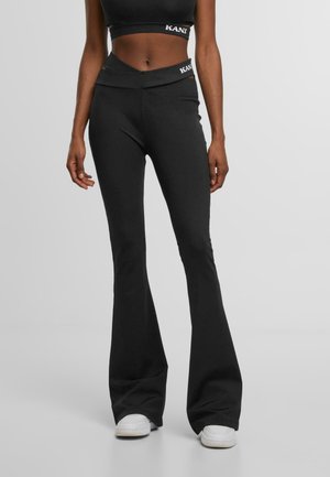 Black flared pants made of stretch fabric, featuring a high waistband with a cross design and logo detail. Smooth texture, fitted shape.