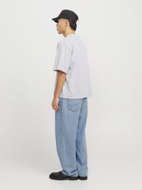 Camiseta gris de manga corta combinada con jeans holgados de color azul claro y zapatos negros. Una gorra negra completa el atuendo informal.