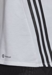 Camiseta blanca de mezcla de algodón, con tres franjas verticales negras en el costado y el logo "AEROREADY" cerca del dobladillo. Textura suave.