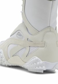 High-top sneakers in white and beige, featuring a combination of leather and mesh materials, textured sole, and distinctive logo detailing.