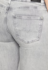 Jeans de mezclilla gris con un bolsillo trasero que presenta un patrón de costura distintivo y una etiqueta de cuero en la cinturilla, textura suave.
