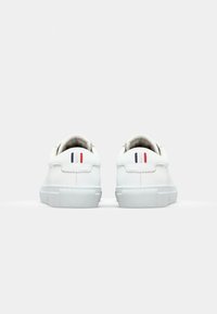 White leather sneakers with a smooth finish, featuring a low-top design and contrasting accent stripes in red, white, and blue on the heel.