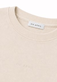 Sweat beige à col rond côtelé avec texte en relief "OH APRIL" sur la poitrine et une étiquette blanche avec le texte "OH APRIL" à l’intérieur de l’encolure.