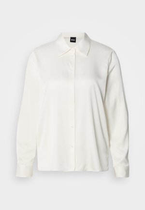 Camicia bianca a maniche lunghe in tessuto liscio, con colletto classico, chiusura frontale con bottoni e polsini con bottoni, dalla vestibilità comoda.