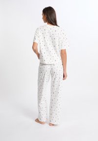 Conjunto de pijama blanco hecho de tela suave, que presenta una parte superior de manga corta y pantalones holgados, ambos decorados con pequeños motivos coloridos.