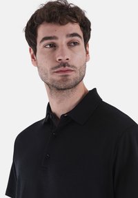 Zwarte polo met een gestructureerde afwerking, drieknoops sluiting en een klassieke kraag. Slank model. Geen zichtbare logo's of patronen.