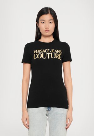 Camiseta de algodón negra de manga corta, con un logo impreso en dorado "VERSACE JEANS COUTURE" en el pecho. Textura suave.