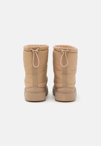 Jasno beżowe buty puchowe z zaciągniętą górą, gładką teksturą i gumową podeszwą. Posiadają tylną szew i uchwyty do łatwego zakładania.