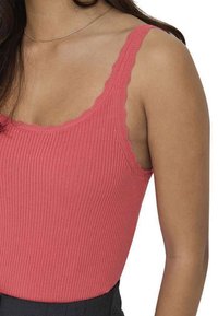 Débardeur côtelé en corail rose, avec des bords festonnés sur les bretelles. Le tissu est en maille douce avec une silhouette ajustée. Idéal pour le superposition.