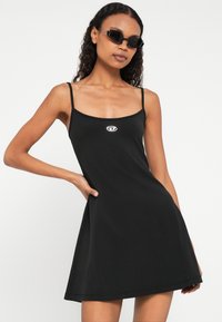 Μαύρο αμάνικο φόρεμα από απαλό ύφασμα, με εφαρμοστό μπούστο και φουσκωτή φούστα. Μικρό λογότυπο στο στήθος, μίνιμαλ σχεδιασμός.