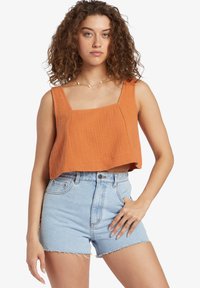 Cropped tank top in textured burnt orange fabric with square neckline; paired with high-waisted denim shorts with frayed hem.