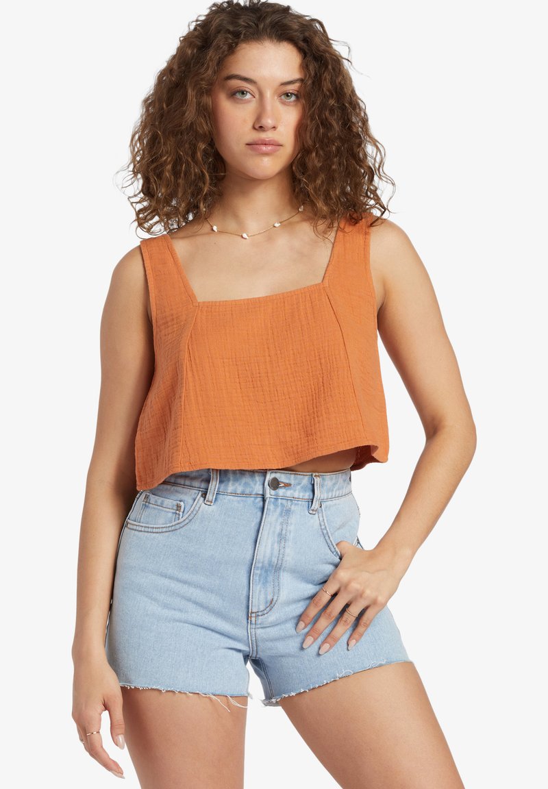 Cropped tank top in textured burnt orange fabric with square neckline; paired with high-waisted denim shorts with frayed hem.