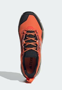 Orange och svarta träningssneakers med mesh-överdel, texturerad detaljering, kontrasterande snören, vadderad tunga och gummiyttersula.