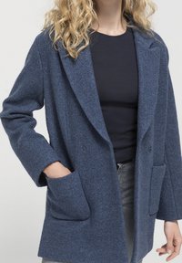 Blå ullblandad kappa med kavajkrage, dubbelknäppt design, två framfickor och en texturerad yta.