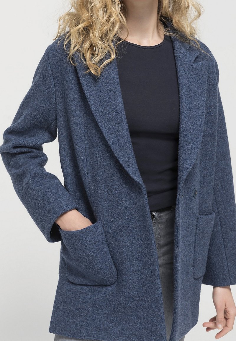 Blå ullblandad kappa med kavajkrage, dubbelknäppt design, två framfickor och en texturerad yta.