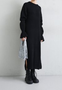 Stickad svart långärmad klänning med utsvängda muddar och slitsar i sidorna, bärs med svarta snörstövlar och en grå nätväska.