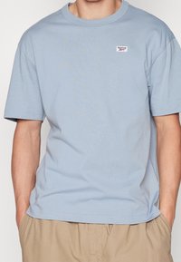 Světle modré bavlněné tričko s krátkým rukávem, kulatým výstřihem a malou nášivkou loga Reebok na levé hrudi. Měkká a hladká textura.