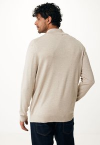 Pullover beige lavorato a maglia con collo a camicia, maniche lunghe e polsini a coste, abbinato a jeans in denim scuro. Tessuto semplice e liscio.