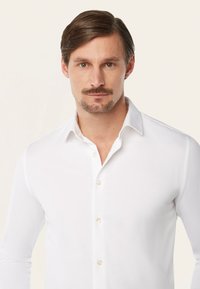 Witte blouse met lange mouwen, featuring een klassieke kraag, een voorpand met parelknoopjes en een gladde katoenen stof. Geen patronen of accenten.