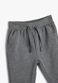 Pantalones de chándal grises con una cinturilla acanalada, cordón y dos bolsillos laterales. Hechos de una tela suave y texturizada con un corte relajado.