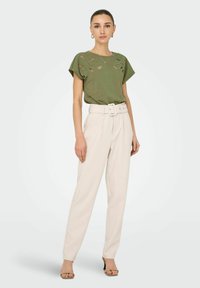 Haut vert olive à manches courtes avec broderie florale, associé à un pantalon crème taille haute et des sandales à talons beiges.