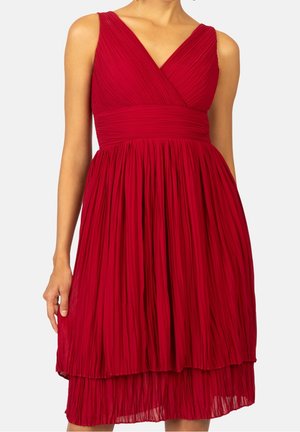 Czerwona sukienka bez rękawów z plisowanym dołem, dekoltem w serek i dopasowaną talią, warstwowa spódnica sięgająca do kolan.