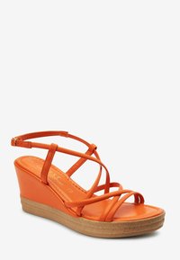 Sandales compensées orange avec des brides fines croisées et une semelle en fibres naturelles. Texture lisse sur les brides, couleur unie sur toute la surface.