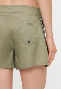 Shorts kaki avec une poche arrière, logo Roxy noir, longueur courte, texture lisse et accent latéral avec un motif léopard.