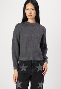 Grå strikkegenser med strukturert overflate, rund hals og ribbestrikket kant. Brukt sammen med svarte jeans med stjernemønster.