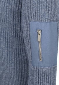 Blauwe gebreide trui met ribstructuur en een effen blauwe paneel met een ritszak op de bovenarm.