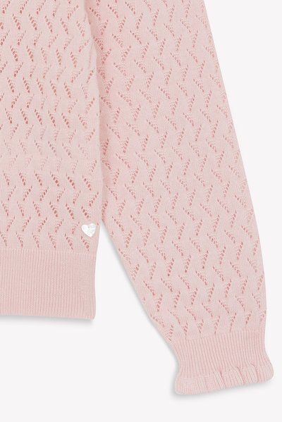 Helle pinke gestrickte Pulloverbündchen mit Zickzack-Durchbrochungsmuster und geripptem Abschluss, ausgestattet mit einem kleinen herzförmigen Metallschild nahe dem Saum.