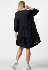 Schwarzes, schichtartiges Kleid mit einem gerippten Textur und Dreiviertelärmel. Hat eine lockere Passform und eine dekorative Borte am Saum. Kombiniert mit weißen Sneakers.