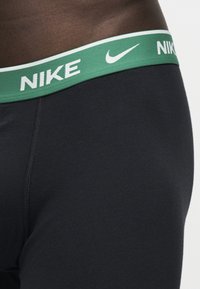 Gros plan d'une personne portant un sous-vêtement noir Nike avec une ceinture verte arborant le logo blanc Nike et du texte.