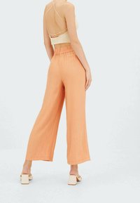 Kevyet, leveälahkeiset housut pehmeästä persikankeltaisesta kankaasta. Niissä on joustava vyötärönauha ja sileä, tekstuuriltaan miellyttävä pinta. Yhdistetty neutraaliin yläosaan.