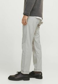 Graue Baumwollhosen mit geradem Schnitt, jeweils mit umgeschlagenen Säumen und kombiniert mit schwarzen Lederschuhen. Weiche Textur und minimalistisches Design.