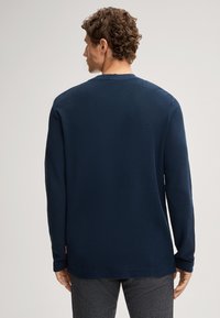 Marineblaues Langarmshirt aus strukturiertem Stoff, mit Rundhalsausschnitt und normaler Passform. Einfarbige Rückseite mit dezentem Markenlabel am Saum.