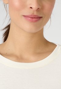 White lightweight top with a round neckline and smooth texture, featuring a subtle ribbed accent around the collar and shoulders.