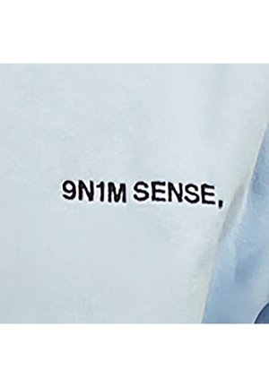 Helles blaues Gewebe mit dem Text "9N1M SENSE" in fetten schwarzen Buchstaben. Die Oberfläche wirkt glatt mit einem leichten Glanz.