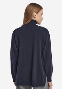 Mörkblå polotröja med avslappnad passform, ribbade muddar och fåll. Mjukt tyg med en slät yta utan synliga mönster eller detaljer.