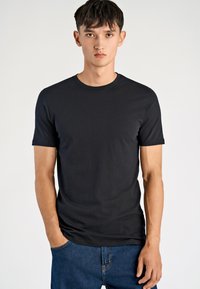 T-shirt nera a maniche corte realizzata in tessuto morbido. Presenta un girocollo e un logo discreto sul petto. Abbinata a jeans di denim blu.