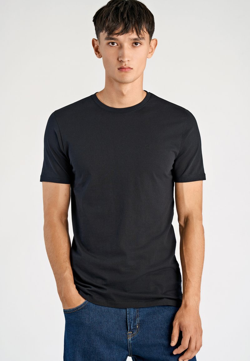 T-shirt nera a maniche corte realizzata in tessuto morbido. Presenta un girocollo e un logo discreto sul petto. Abbinata a jeans di denim blu.