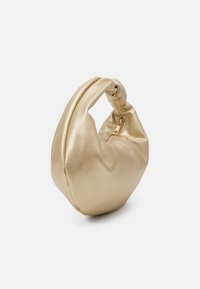 Sac à main en or métallique doux avec une poignée nouée et une fermeture éclair dorée visible, présenté sur un fond blanc.