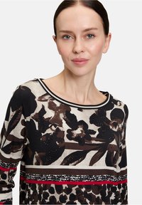 Maglietta a maniche lunghe in tessuto leggero con stampa floreale e leopardata nei colori marrone, nero e crema, arricchita da dettagli rossi e bianchi e da paillettes incorporate.