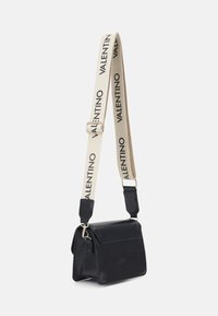Black crossbody bag with a textured exterior and structured design. Features a cream strap with "VALENTINO" in bold black lettering.
