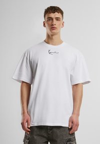 T-shirt en coton blanc à manches courtes, avec un petit logo noir sur la poitrine. Coupe confortable, col rond et texture lisse.